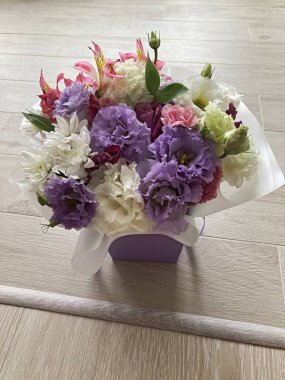 Bir buket çiçekli bir sepet. Güller ve kasımpatılar pembe arka planda bir sepette.