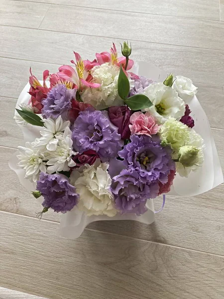 Bir buket çiçekli bir sepet. Güller ve kasımpatılar pembe arka planda bir sepette.