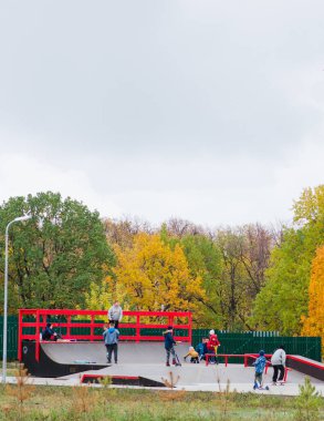 Çocuklar sonbaharda paten parkında bisiklete, kaykaya, scooterlara binerler.