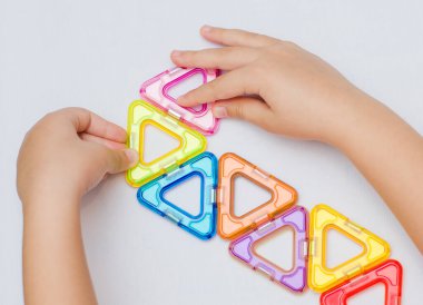 5 yaşındaki bir çocuk, manyetik bir yapıcının çok renkli parçalarından geometrik şekiller toplar. Düz yatıyordu
