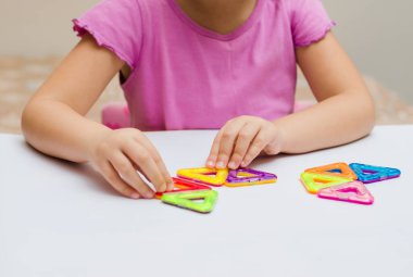 5 yaşındaki bir çocuk, manyetik bir yapıcının çok renkli parçalarından geometrik şekiller toplar. Düz yatıyordu