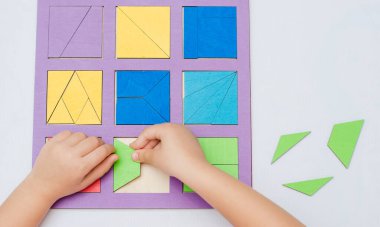 Çocuk, kareli bir tahtada çok renkli geometrik şekiller topluyor.