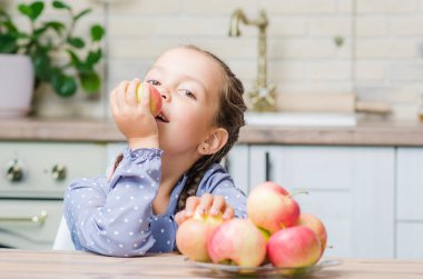 Güzel bir mutfakta, beş yaşında bir kız elinde olgun elmalarla masada oturuyor.