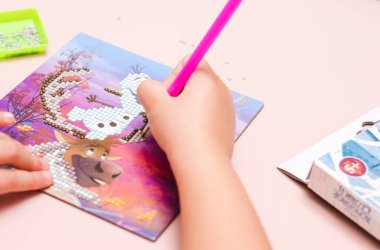 Elmas mozaiği. Çocuk sahte elmasları cımbızla desene göre tuval üzerindeki numaralara göre seriyor.