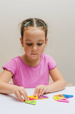 5 yaşındaki bir çocuk, manyetik bir yapıcının çok renkli parçalarından geometrik şekiller toplar..
