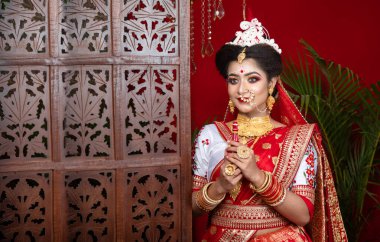 Zarif bir gelinlik içinde güzel bir Bengali gelinin portresi. Gelinlik takıları ve bilezik makyajıyla. Muhteşem sari salonunun içinde ağır süslemeleri var. Duygusallık ve cazibe. Geleneksel Bengali Sarisi ve Mücevherleri 'nde güzel yetişkin gelin.