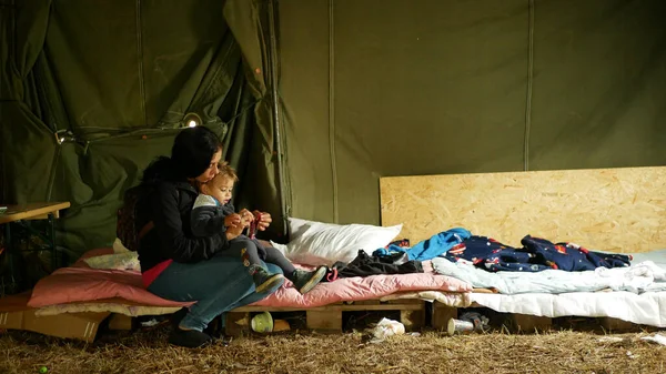 移民難民ウクライナの母親と赤ちゃんの食事 テントの中で貧困パレットとマットレスジプシーキャンプの人々家族の子供ベビーカー子供ローマの祖母と孫食べる — ストック写真