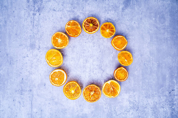 Christmas wreath or Advent crown minimalism: dried orange slices in bright colors, arranged in a circle on a background with concrete look. Table top view, flat lay, copy space.