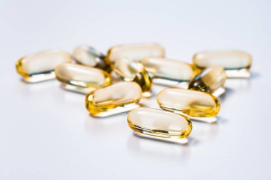 Altın sarısı yumuşak kapsüller beyaz arka planda ışığı yansıtıyor. İlaç, uyuşturucu, beslenme veya beslenme takviyesi kavramı.