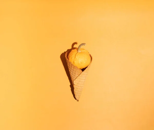 Pumpkins in the wafle cone ice-cream cone on autumn colors background. Autumn and sweet dessert. Minimal Holiday Halloween   concept.