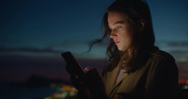 若い女性は日没の光の中で電話を見て — ストック動画
