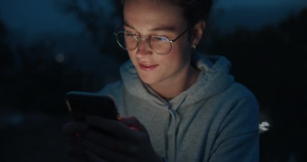 Młoda kobieta patrzy na telefon w świetle zachodu słońca — Wideo stockowe