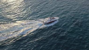 Mavi okyanus suyunda gezen lüks beyaz yatın yan görüntüsü. Bir grup arkadaşla gün batımına doğru yelken açarken özel motorlu yelkenlinin drone çekimi. Akdeniz gezisi