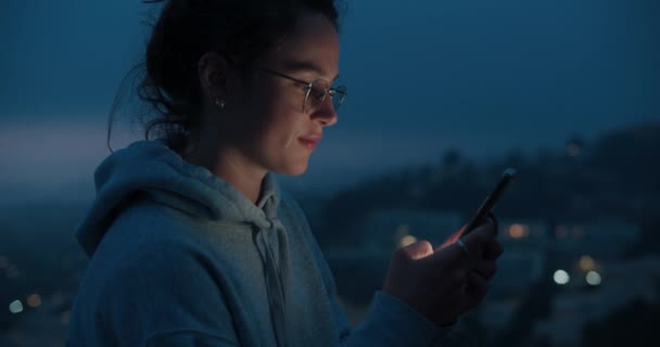Giovane donna guarda il telefono alla luce del tramonto — Video Stock