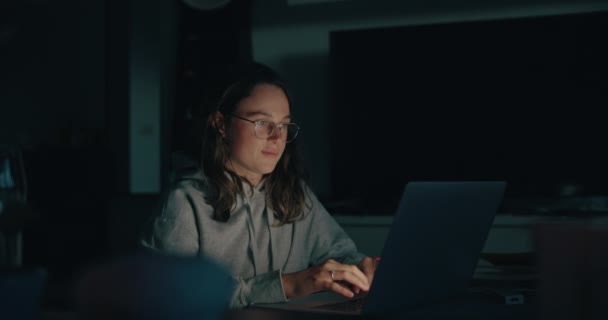 Настоящая молодая женщина работает на ноутбуке в темном доме — стоковое видео