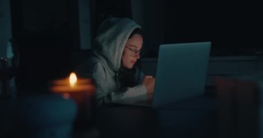 Otantik genç kadın karanlık evde dizüstü bilgisayarda çalışıyor.