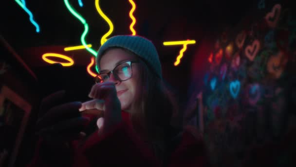 Genç kadın şehir merkezindeki neon sette telefon kullanıyor. — Stok video
