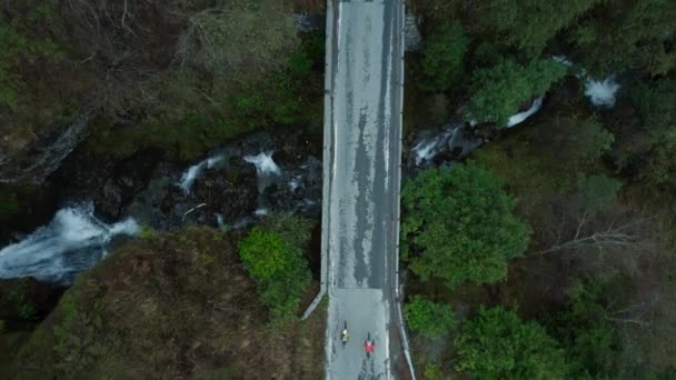 Scenic aerial drone shot of two cyclists on bridge — Vídeo de Stock