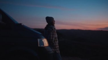 Cinematic lens view, soft blurry focus on young lonely woman, traveler watching colorful stunning Porto sunset, leaning on adventurous camper van, dreaming about happy carefree future life near ocean