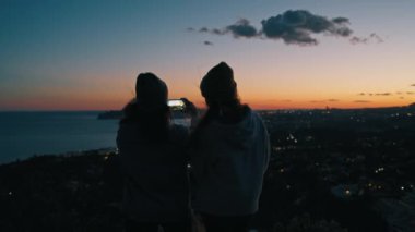 Genç kadınlar, milenyum kızları, arkadaş silueti renkli, karanlık, günbatımı, panoramik, panoramik fotoğraf çeken telefonları bir arada tutan, hafta sonu kamerayla gezen, seyahat eden, tatile çıkan kızlar.
