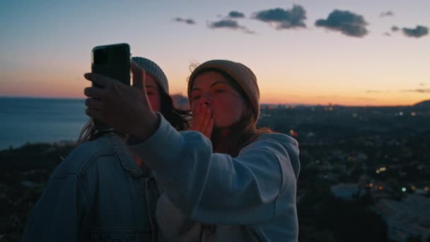 Young millennial cheerful women takes happy selfie, video chatting with friends, sending kisses, flirting, using frontal camera on smartphone during outdoor camping trip near sea, ocean on sunset — Stock Footage Young Millennial Cheerful Women Takes Happy Selfie Video Chatting Friends Royalty Free Stock Video
