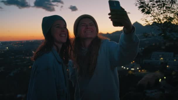 Young millennial cheerful women takes happy selfie, chats by video with friends, sending kisses, flirting, using frontal camera on smartphone, posing on outdoor camping trip near sea, ocean on sunset — Stock Footage Young Millennial Cheerful Women Takes Happy Selfie Chats Video Friends Royalty Free Stock Video