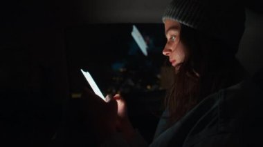 Genç ve çekici bir kadın gece taksi arabasıyla geziyor, cep telefonunu tutuyor, cep telefonunu kontrol ediyor, akıllı telefon kullanıyor, sosyal medya haberlerini çekiyor, e-posta mektuplarını okuyor, mesajları okuyor, internetten alışveriş yapıyor.