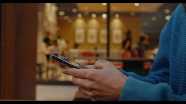 密切关注年轻女性的侧面形象 学生们手握手机 使用智能手机 在社交媒体上与朋友聊天 坐在户外 背对着咖啡馆的灯光 — 图库视频影像