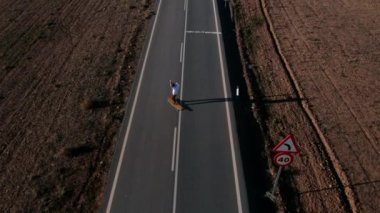 Amerikan kırsalındaki boş bir yolun ortasında, uzun panoda gezmekten hoşlanan, genç bir adamın havadan insansız hava aracı görüntüsü. Yaz zamanı seyahat arzusu ilham, seyahat hayali varış yeri
