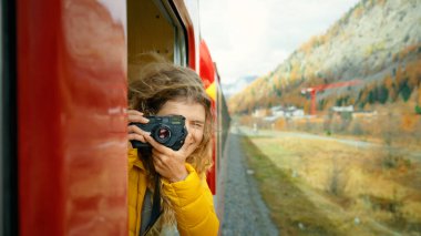 İlham verici kadın gezgin ve seyahat blogcusu sinematik güzel dağlardaki turist treninin camından dışarı bakıyor. Genç ve güzel bir kadın kırmızı trenin penceresinden sarkıyor. Heyecanlı dünya kaşifi