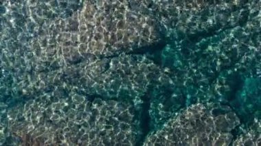 Top aerial drone view on shimmering crystal clear turquoise water over rock bed. Beautiful paradise cove in mediterranean sea or pacific ocean. Beautiful nature background 