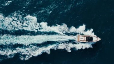 Top view slow motion drone shot of luxury motorboat in ocean waters near marina. Panning shot of yacht swim and raise waves in open blue waters. Amazing epic background over waves in sea