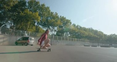 Camera follows beautiful and happy young woman in white shorts effortlessly cruising on sunny morning. Woman is training her surf skills on solid ground. urban extreme sports