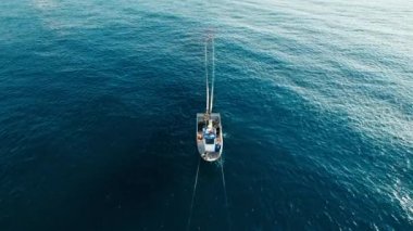 White small fisherman boat with people on board waving in ocean. People work together to pull out trawl with caught fish from deep blue waters. Aerial frontal shot with object in center