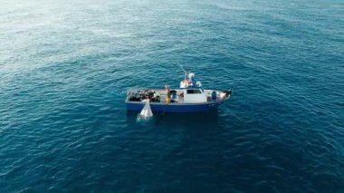 Effective team work of fisherman crew pulling out trawl with sardines from deep blue sea on their vessel. Aerial shot, early morning, alone in ocean