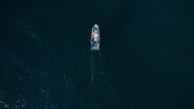 Top view on small trawler boat moving in ocean with deep blue water. Fishermen ready to pull trawl net on board