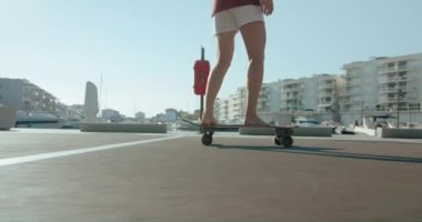 Side fast tracking on woman in white shorts barefoot pushing off ground and accelerating next to the summer houses at resort residence town on seashore. handheld shot with light leaks in frame 
