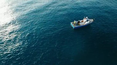 Fishermen pulling out net with caught sardines on their small trawler boat waving in ocean waves. Effective teamwork. Aerial diagonal shot with direct sun light in corner