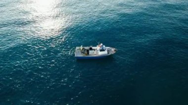 Fishermen at work in the early morning on their small trawler boat waving in open sea. Pulling out trawl with fish from ocean. Aerial side shot