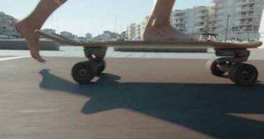 Side fast tracking close-up on feet of young millennial woman in white shorts skateboarding barefoot in the city. Enjoying the moment of summer vacation balancing on surfskate