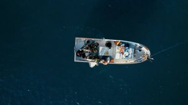 Fishers pulling out netting bags with sardines from sea in plastic buckets on their trawl ship. Aerial top view