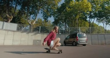 Attractive woman trains her surfing skills in sunny morning on skateboard. Perform sharp turn sitting on board and cruising away with joy. Inclusive and gender friendly urban sport