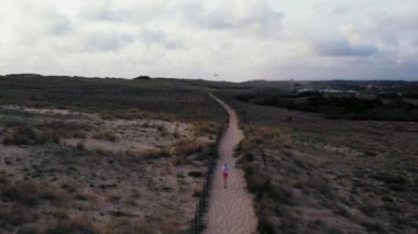Follow tracking shot of athletic woman is running fast between sand dunes at sunset. Evening workout routine. Moody cloudy weather. High quality 4k footage
