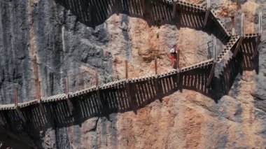 Young female adventurer hike on traitorous and dangerous hiking trail, suspension bridge or wooden track on side of cliff or mountain. Adrenaline adventure in wild secluded place