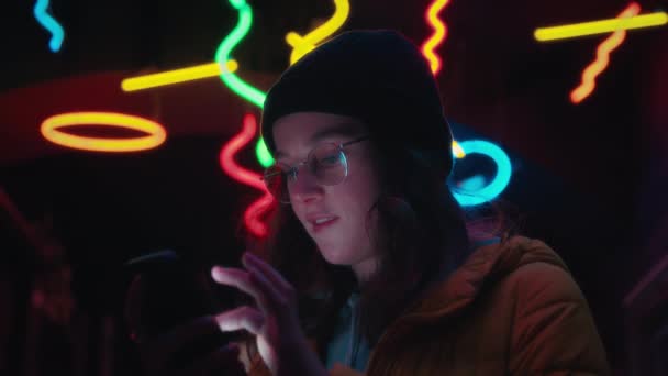 年轻美丽的千禧年女性在智能手机上翻阅应用程序和页面 在屏幕上闪烁着灿烂的面部表情 真实和真实的人使用技术 大城市背景下的霓虹灯 — 图库视频影像