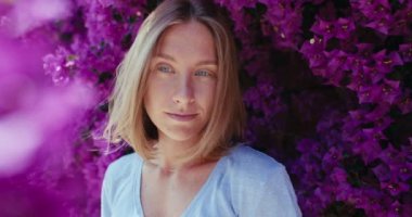 Gerçek, otantik, güzel, parlak mavi gözlü genç bir kadının inanılmaz görüntüsü çiçek çiçeklerinin arasında duruyor. İnanılmaz renkli doğa ve insani duygular. Yaz günü mutlu bir gülümseme.