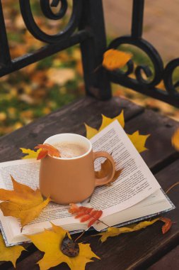 Sarı yapraklı bir kitabın üzerinde bir fincan kahve.