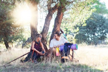 İki yürüyüşçü, bir ağacın gölgesinde dinlenen ve uzun bir yürüyüşten sonra sohbet eden kadın ve erkek.. 