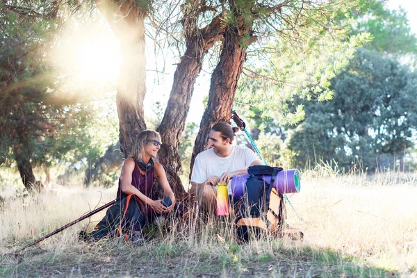 İki yürüyüşçü, bir ağacın gölgesinde dinlenen ve uzun bir yürüyüşten sonra sohbet eden kadın ve erkek.. 