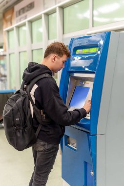 Arka sayfası olan genç bir adam metro istasyonundaki bir otomattan bilet alıyor.